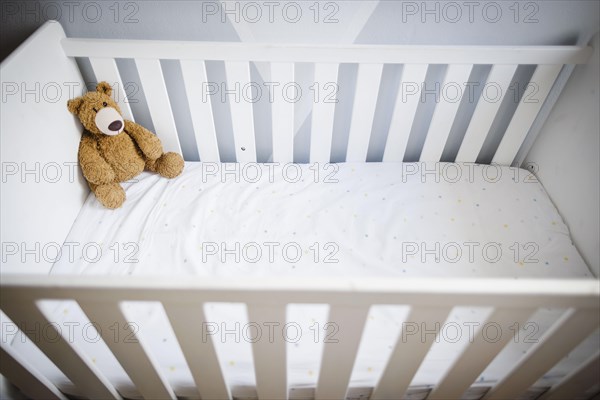 Symbolic photo on the subject of wanting a child. A teddy bear sits in an empty cot. Berlin