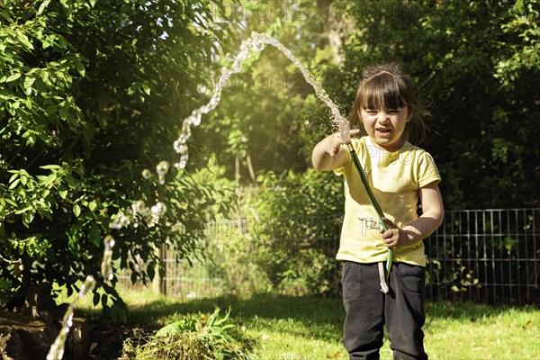 Happy little girl playing with a garden hose. Preschool child having fun with watering trees and plants in domestic garden