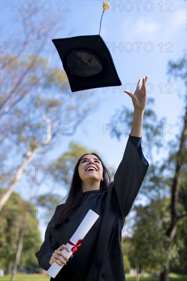 Happy caucasian graduated girl in a black gown throwing the mortarboard to the sky