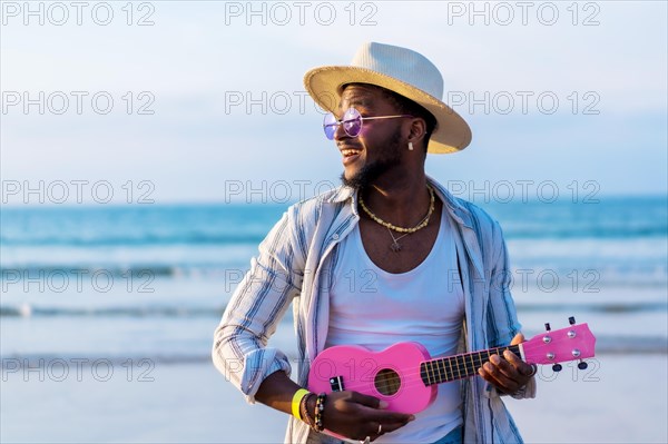 Black ethnic man playing ukulele by the sea enjoying summer vacation on the beach