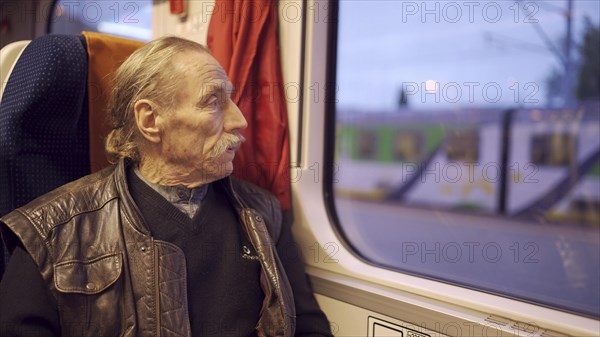 Close up of senior with glasses travels in a train and looks at out the window