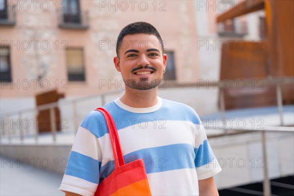Portrait of smiling gay man with rainbow lgbt bag in the city