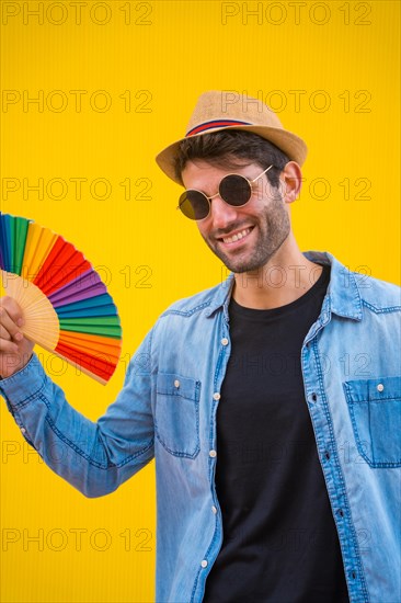 Portrait of a caucasian man in a hat with a rainbow lgbt fan on a yellow background