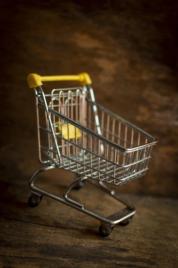 Empty metal miniature shopping cart on a brown background