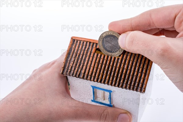 Hand dropping coin into the moneybox in the shape of a model house