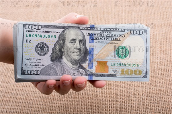 Hand holding banknote bundle of US dollar on a linen canvas background