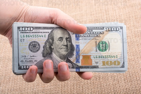 Hand holding banknote bundle of US dollar on a linen canvas background