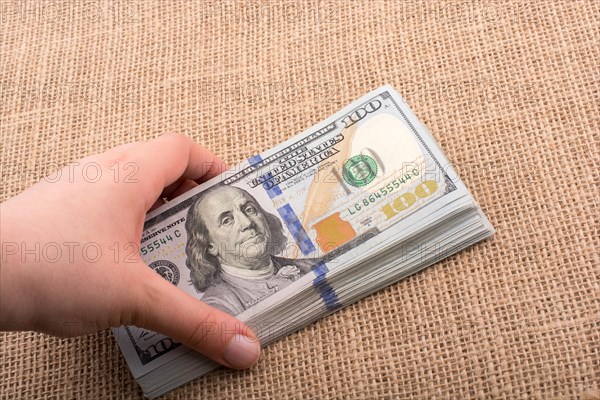 Hand holding banknote bundle of US dollar on a linen canvas background