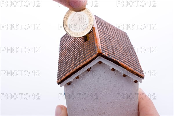 Hand dropping coin into the moneybox in the shape of a model house