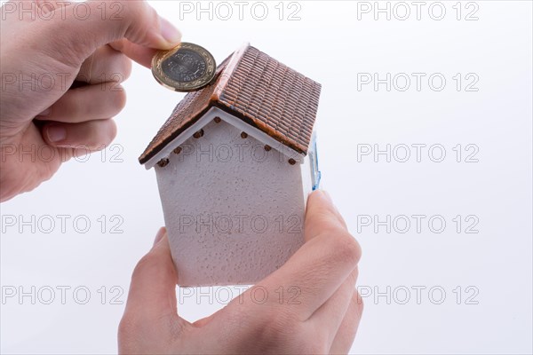 Hand dropping coin into the moneybox in the shape of a model house