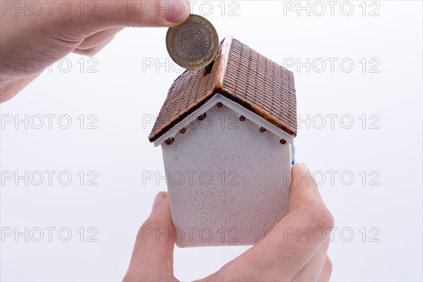 Hand dropping coin into the moneybox in the shape of a model house