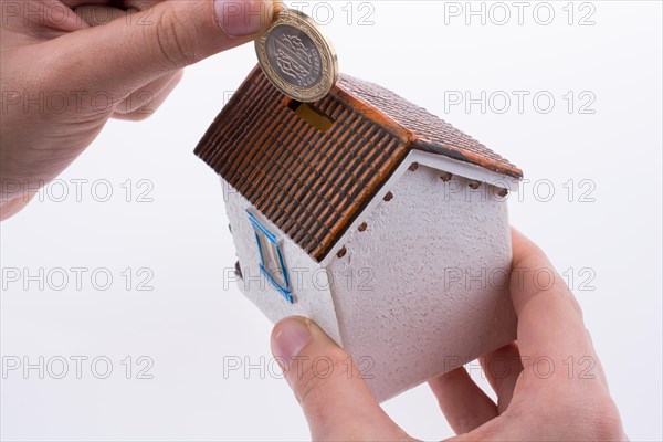 Hand dropping coin into the moneybox in the shape of a model house
