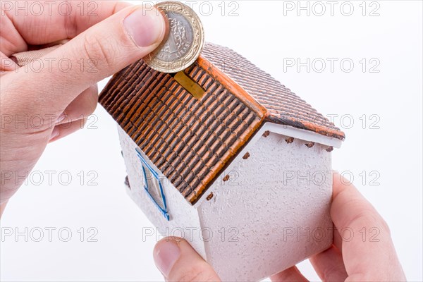 Hand dropping coin into the moneybox in the shape of a model house