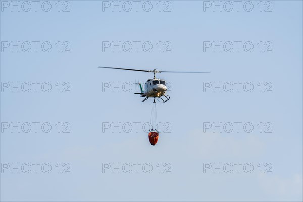 Firefighting helicopter in mid-flight dropping water bag on flames