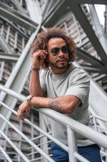 Young man with afro hair wearing sunglasses on the stairs in the city