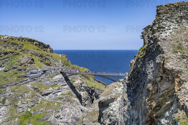 Tourists walk across the new footbridge to the peninsula with the castle ruins of Tintagel Castle