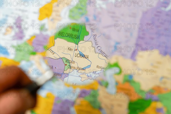 Hand of a man holding a magnifying glass looking at ukraine on a map of the world