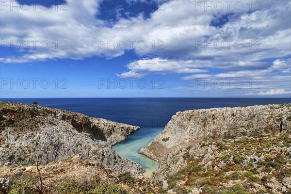 Beautiful view of z-shaped cove or harbor in typical hills of Crete landscape. Clear blue sky and beautiful clouds on sunny day. Azure sea waters. Stefanou beach