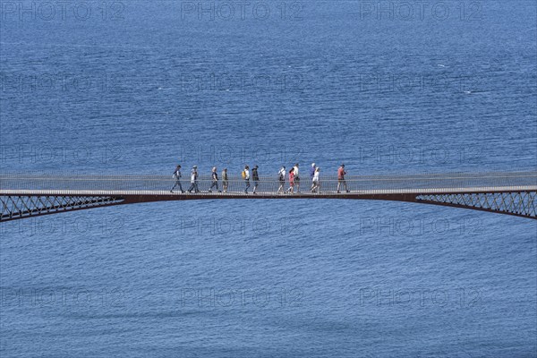 Tourists walk across the new footbridge to the peninsula with the castle ruins of Tintagel Castle