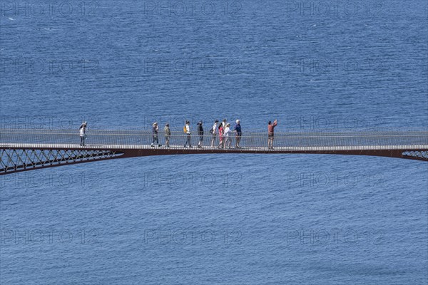 Tourists walk across the new footbridge to the peninsula with the castle ruins of Tintagel Castle