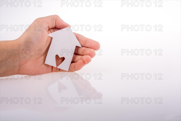 Hand holding a paper house with a heart carved in it on a white background