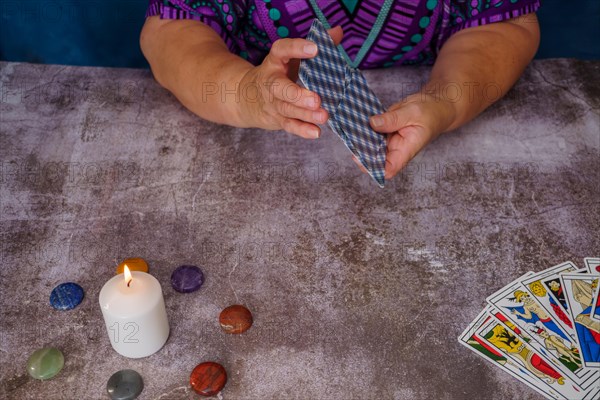 Woman shuffling tarot cards on a table with candles and chakra stones