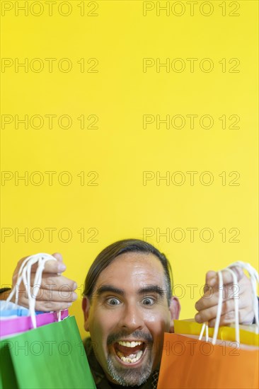 Happy smiling man holding shopping bags on yellow background. Joy of consumption. Purchases