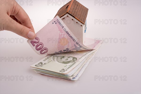 Hand holding Turkish Lira banknotes by the side of a model house on white background