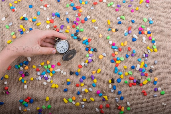 Pocket watch amid colorful pebbles on canvas background