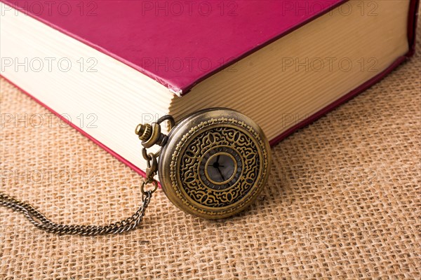 Retro style pocket watch beside a book on a canvas