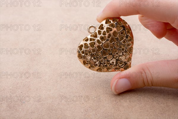 Heart shaped gold color metal object in hand