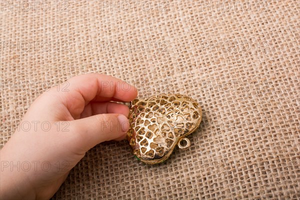 Heart shaped gold color metal object in hand