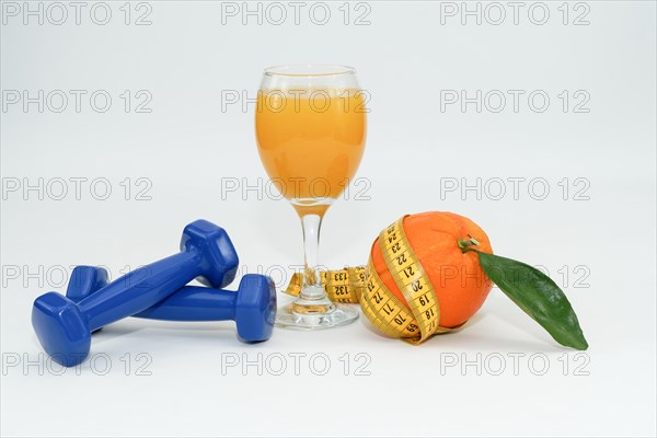 Orange with leaves surrounded by a tape measure with dumbbells and a glass of fresh orange juice