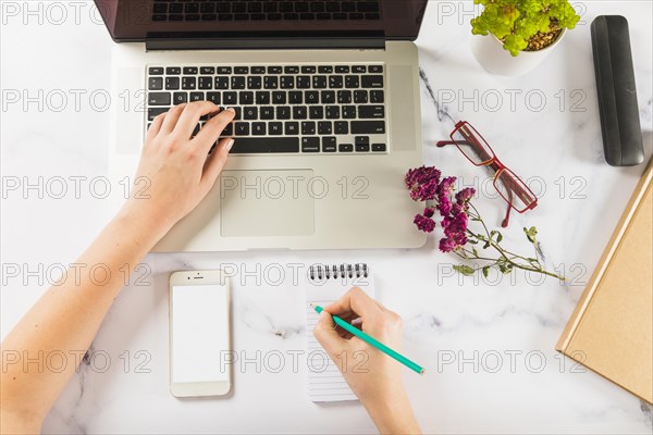 Crop hands using laptop making notes marble table