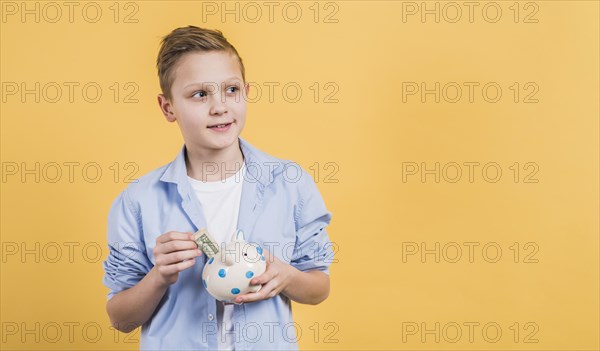 Smiling boy inserting currency note ceramic white piggybank