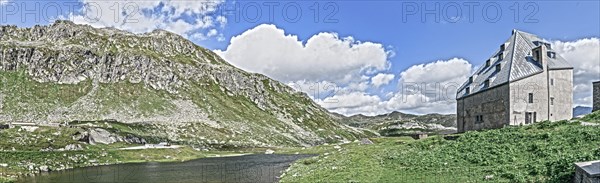 Photo with reduced dynamics saturation HDR of view on left mountain lake right historical hotel accommodation Ospizio San Gottardo Sankt Gotthard Hospice with historical building fabric from year 1237...
