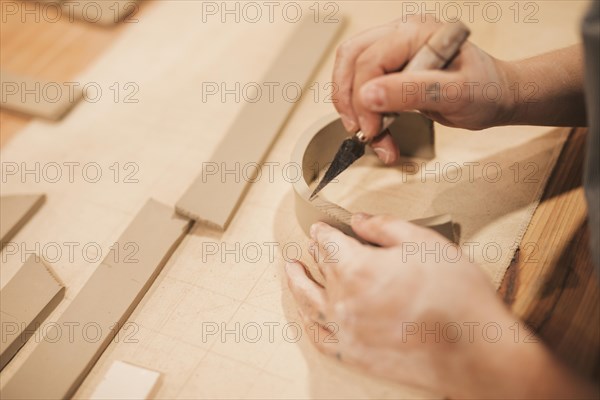 Female potter s hand engraving clay with tools wooden table