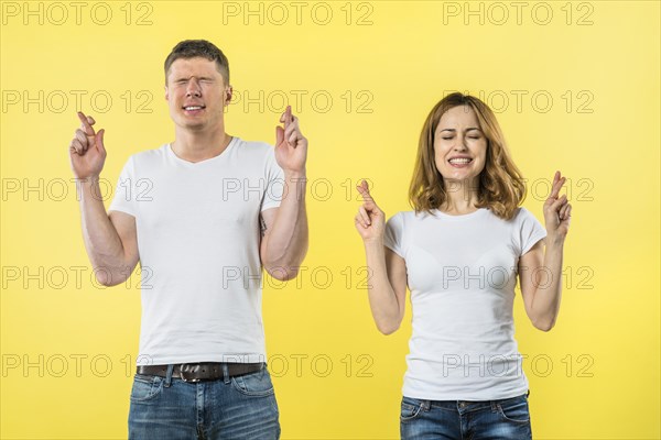 Smiling young couple crosses fingers anticipation something pleasant