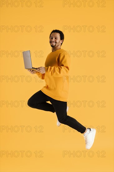 Portrait young man jumping with laptop