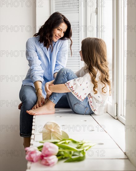 Happy mother daughter sitting window sill