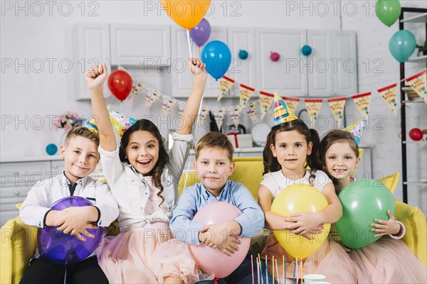 Portrait children sitting sofa holding balloons