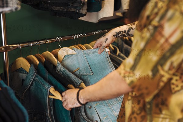 Close up man s hand choosing blue jacket hanging rail clothing shop