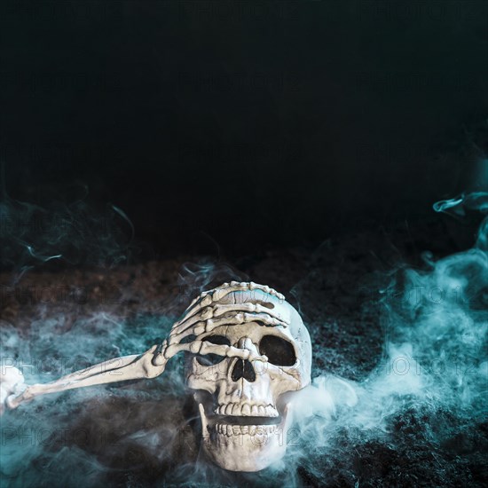 Skeleton s hand touching skull blue fog ground