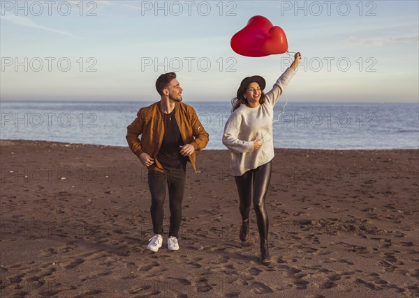 Happy couple running sea shore with heart balloons