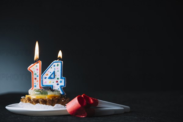 Number 14 birthday lighted candle slice tart party horn blower against black backdrop