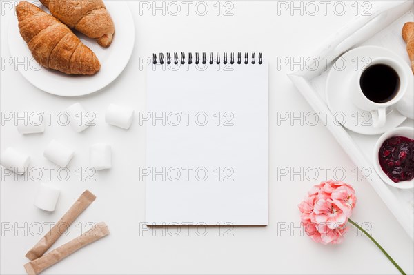 Notebook beside tray with cup coffee croissant