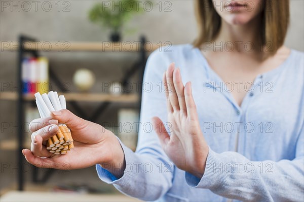 Woman showing stop gesture holding bunch cigarettes hand