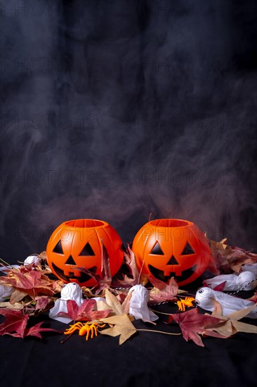 Halloween pumpkins over red autumn leaves and ghosts with smoke on a black background