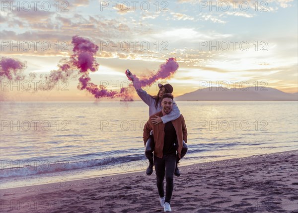 Man holding woman with pink smoke bomb back sea shore