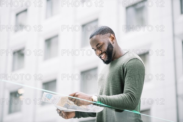 Smiling man reading newspaper near glass fence